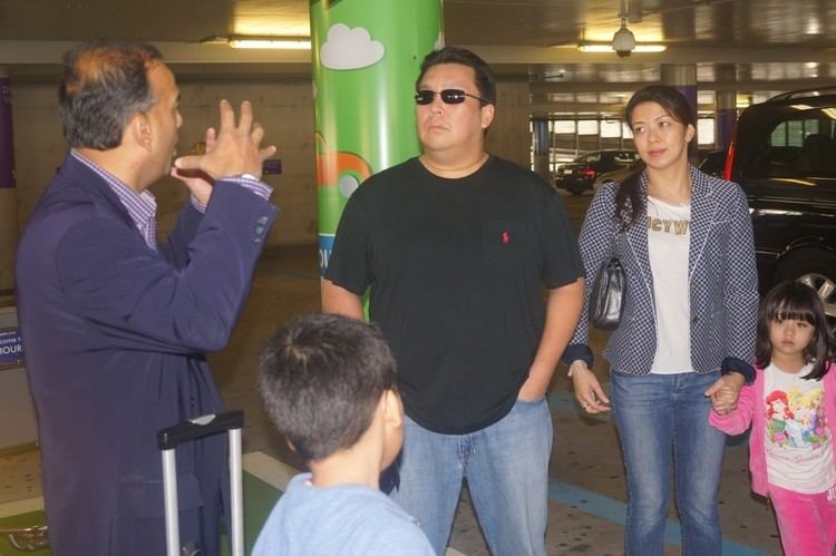 Tunku Abdul Majid wearing sunglasses and a black shirt, his wife wearing a blue coat and a white shirt, and his daughter wearing a pink jacket with a man wearing a blue suit.