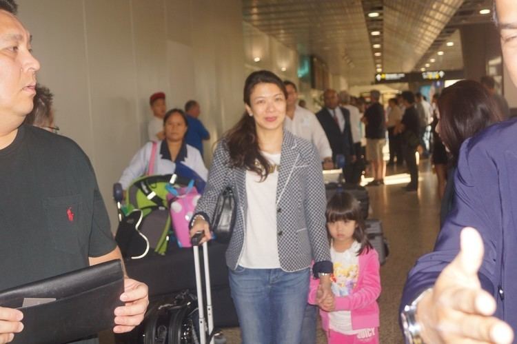 Tunku Abdul Majid wearing a black shirt with his wife carrying luggage and his daughter wearing a pink jacket at the airport.