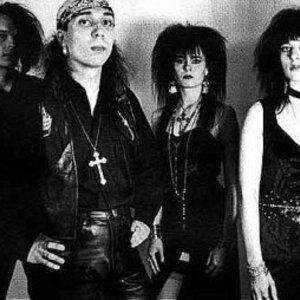 Anne Nurmi and Nauku (right) of Two Witches along with their two other bandmates (left). The man on the left with a fierce look is wearing a bandana, earrings, a cross necklace, pants, t-shirt under a jacket while Anne Nurmi and Nauku wearing a dress, necklace, bracelet, and earrings