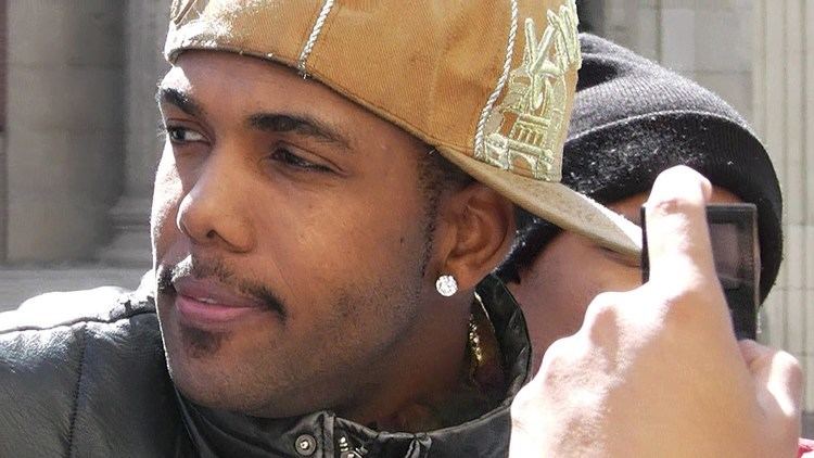 Tyrone D. Burton looking afar while wearing brown cap, black jacket and earrings