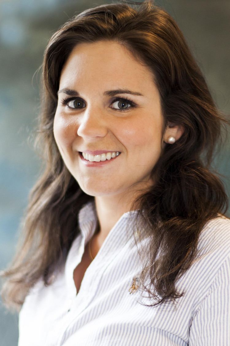 Ulrika Bergman smiling in her wavy hair and wearing a white striped blouse with a pearl earrings