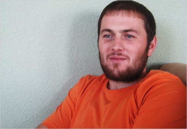 Umar Israilov smiling with a beard and mustache while wearing an orange shirt