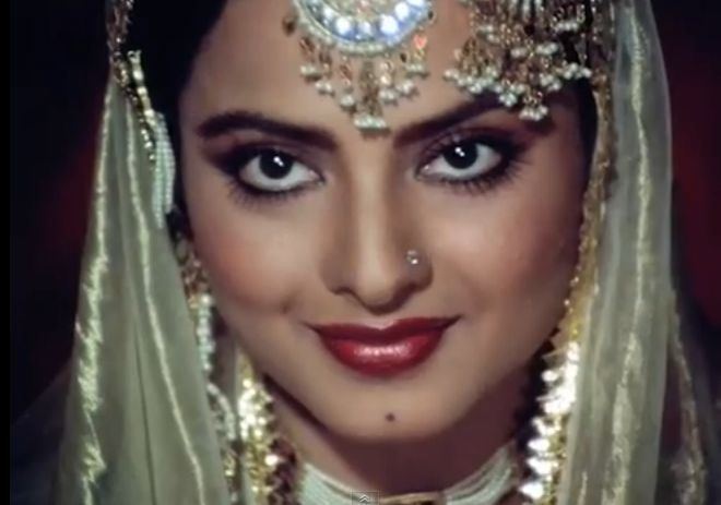 Rekha as Umrao Jaan smiling and wearing a yellow veil with some hair ornaments