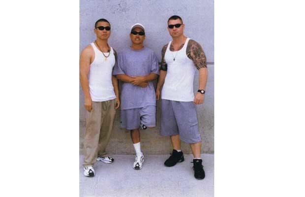 The United Nations gang founder Clayton Roueche wearing black shades and a sleeveless shirt with the two men beside him