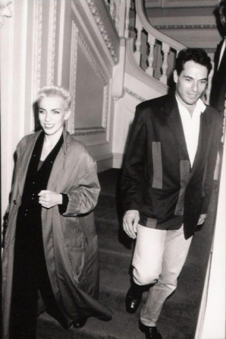 Annie Lennox smiling while walking down the stairs and wearing a long coat and Uri Fruchtmann wearing a coat, long sleeves, and pants