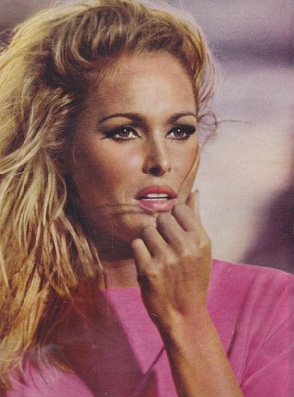 Ursula Andress posing for a publicity photo with her hand in her mouth and wearing a pink shirt for Dr. No, 1962.