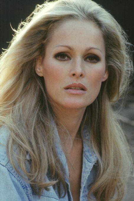 Ursula Andress half smiling and wearing a light blue jean jacket with her hair drawn back.