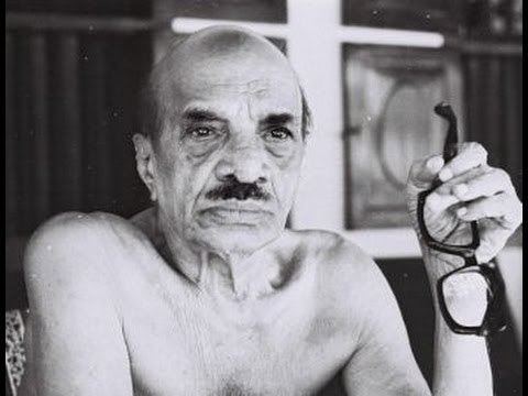 Vaikom Muhammad topless holding pair of eyeglasses while sitting inside a room (black and white photo)