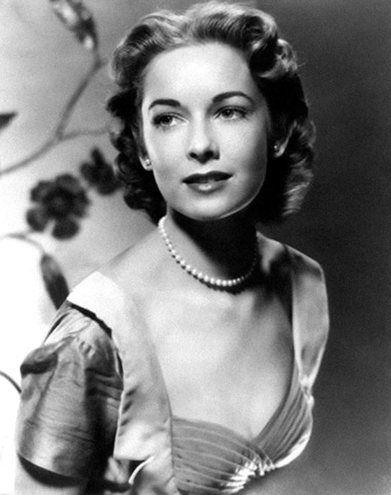 Vera Miles smiling and looking on another side while wearing a dress paired with pearl earrings and necklace