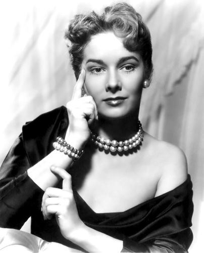 Vera Miles smiling in a pose while wearing a black dress and pearl accessories