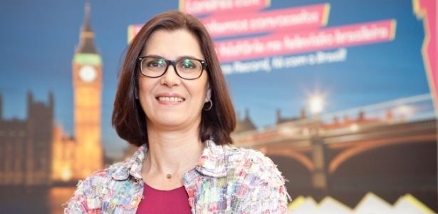 Vera Mossa smiling while wearing a colorful blazer, pink-violet inner blouse, eyeglasses, earrings, and necklace