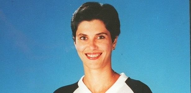 Vera Mossa smiling while wearing a black and white t-shirt, necklace, and earrings