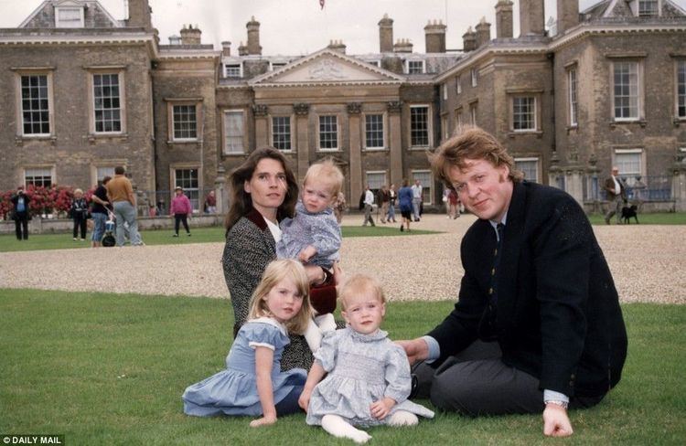 Victoria Aitken and Charles Spencer together with their children sitting on the ground with a big house at their back.