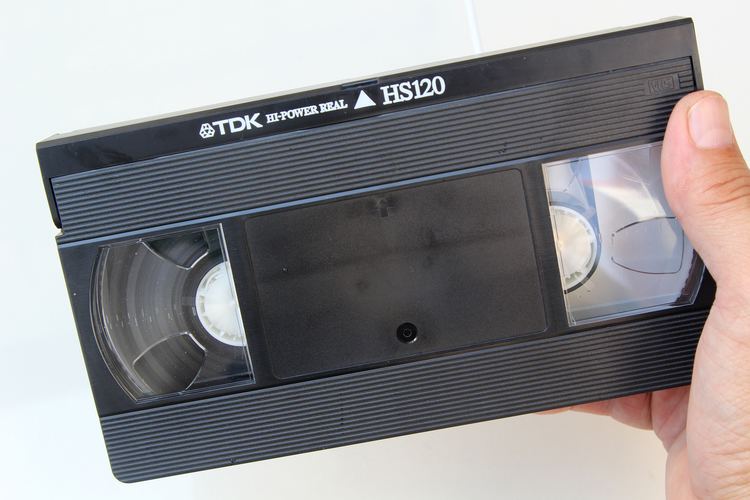 A hand holding a black videotape.