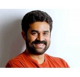 Vijay Babu smiling with mustache and beard while wearing an orange t-shirt