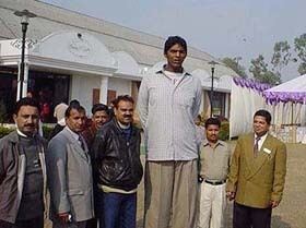 Vikas Uppal posing in the middle of people and wearing a light gray buttoned shirt and light brown pants.