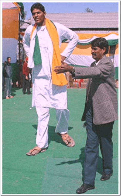 Vikas Uppal walking while being led to something and wearing a white Dhoti with an orange and green scarf.