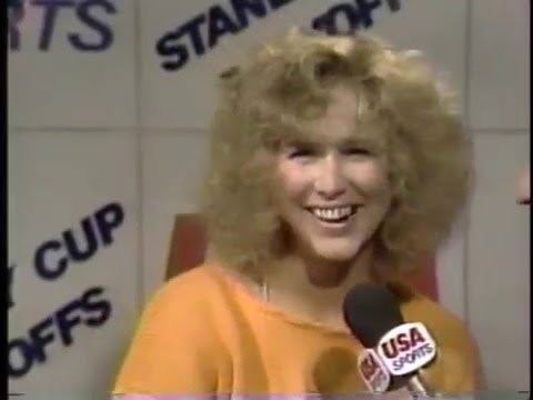 Vikki Moss smiling in an interview by USA Sports, she has blonde kinky hair, wearing an orange shirt