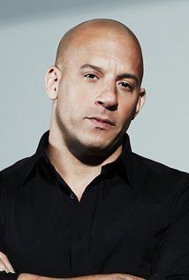 Vin Diesel posing with his arms crossed and wearing a black polo shirt.