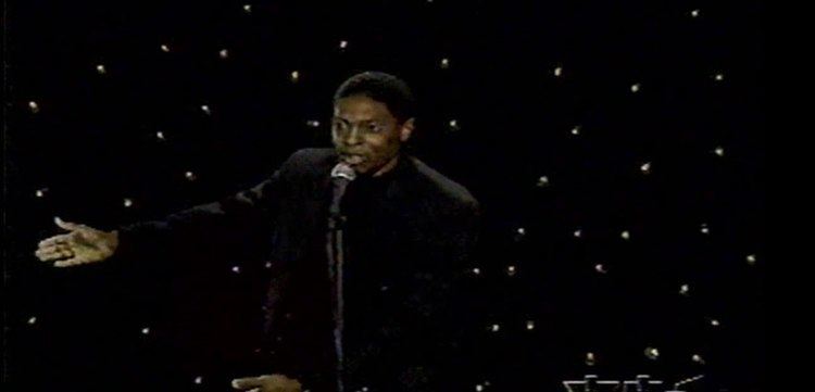 Vinson Horace Champ wearing a black coat with a microphone in front of him.