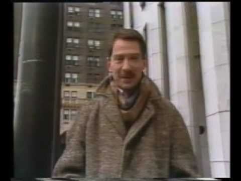 Vincent Hanley reporting with a building in the background, having a mustache and wearing a brown coat and scarf