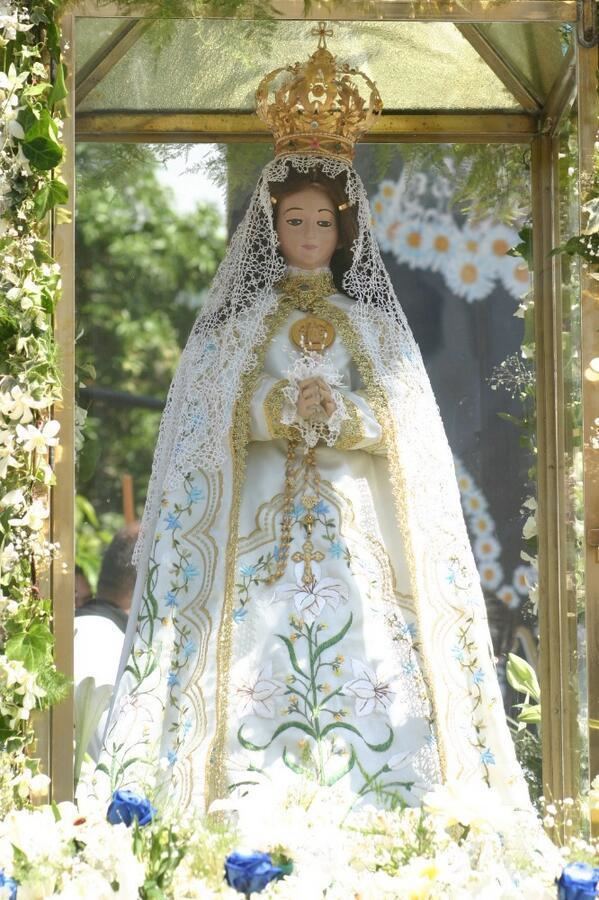 Statue of Virgen del Valle in a glass box while holding a rosary and wearing a crown, white veil, white and gold floral dress, and cape