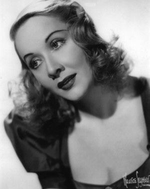 Vivian Vance is serious while looking to the left, mouth half opened, has short curly hair, wearing a black cleavage showing top.