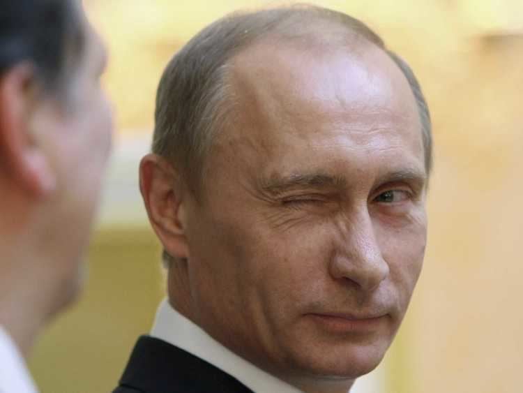 Vladimir Putin is winking at the man beside him. Vladimir is wearing a black coat over white long sleeves.