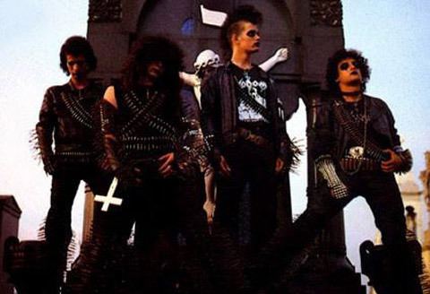 Wagner Lamounier posing with his bandmates and they are wearing a black shirt, spiked gauntlets, black pants, and bullet belt