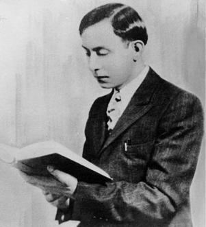 Wallace Fard Muhammad reading a book with a serious face while wearing a long sleeve under a necktie and coat