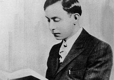 Wallace Fard Muhammad reading a book with a serious face while wearing a long sleeve under a necktie and coat