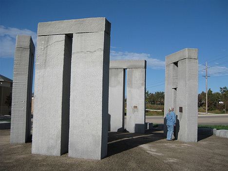 Wally Wallington posing with a recreation of the Stonehenge and wearing a sky blue shirt.