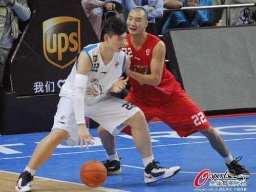 Wang Zhelin playing basketball while wearing a white and blue jersey and Nike rubber shoes