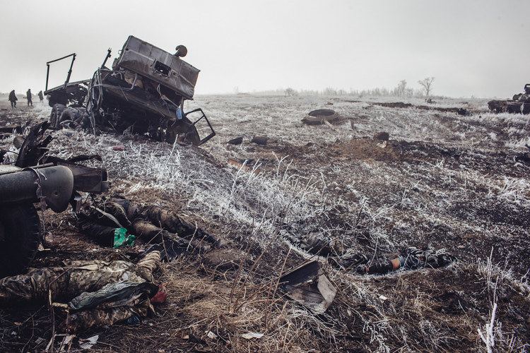 Destroyed Ukraine military vehicle with dead Ukraine soldiers lying o the ground and three people are walking in the field on the outskirts of Debalstseva, 2014