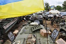 A BTR-80 in Ukrainian service with other tanks and two groups of Ukraine soldiers talking to each other while wearing Army Combat Uniform