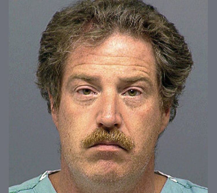 Ward Weaver with a serious face, furrows on the forehead, golden-gray hair, and a mustache while wearing a blue shirt