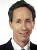Warren Jeffs is smiling and has black hair, wearing a white polo with a black necktie under a black coat