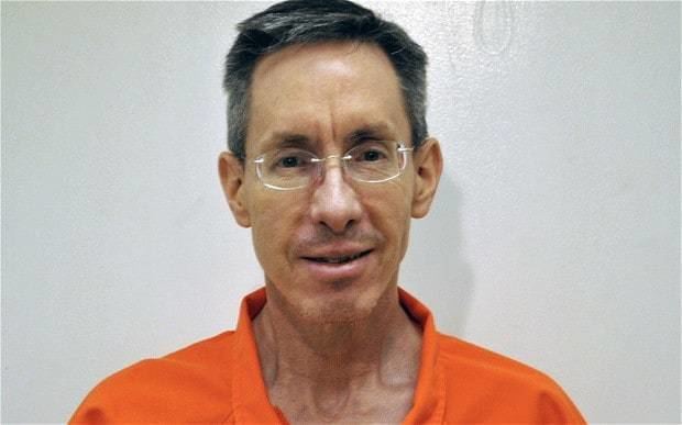 Warren Jeffs is smiling with his black hair and a mustache wearing eyeglass, and an orange polo