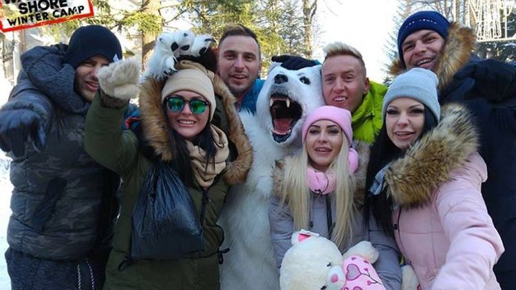 The cast of Warsaw Shore smiling all together with the white bear mascot while they are wearing a winter jacket