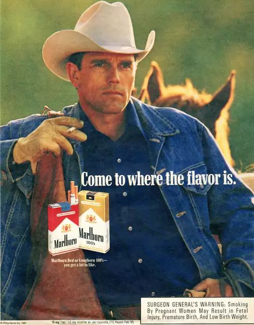 The advertisement poster of Marlboro, Wayne McLaren is serious, standing with a horse at the back, right arm up leaning to his right while holding a cigarette with his right hand using his index and middle finger, has black hair, wearing a white cowboy hat, dark blue polo, brown gloves and a blue denim jacket, in front is a wording written ‘’Come to where the flavor is.’’ with red and gold packs of cigarette, at the bottom is a word written ‘’ SURGEON GENERAL’S WARNING, Smoking By Pregnant Women May Result in Fatal Injury, Premature Birth, and Low Birth Weight’’