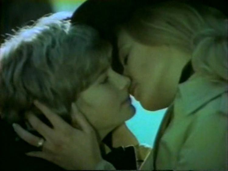Mark Lester and Britt Ekland in a kissing scene while Britt is wearing a black hat, ring and beige blouse from the 1971 horror film, What the Peeper Saw