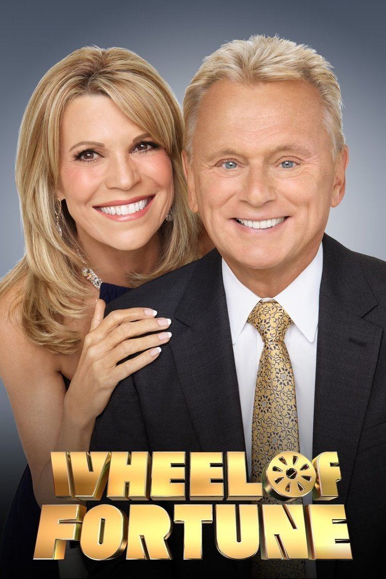 Hosts of Wheel of Fortune Vanna White and Pat Sajak are smiling while Vanna holding Pat's shoulder. Vanna with blonde hair, wearing earrings, a necklace, and a black tube dress while Pat is wearing a black coat over white long sleeves, and a golden floral tie.