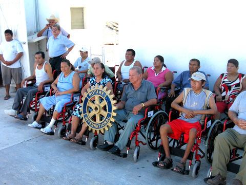 A group of wheelchair users sitting on their wheelchairs while the two at the center, holding a logo of rotary international
