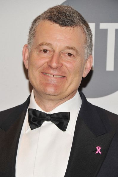 William P. Lauder smiling while wearing a black coat with a small pink ribbon on the right side, white long sleeve, and black bow tie