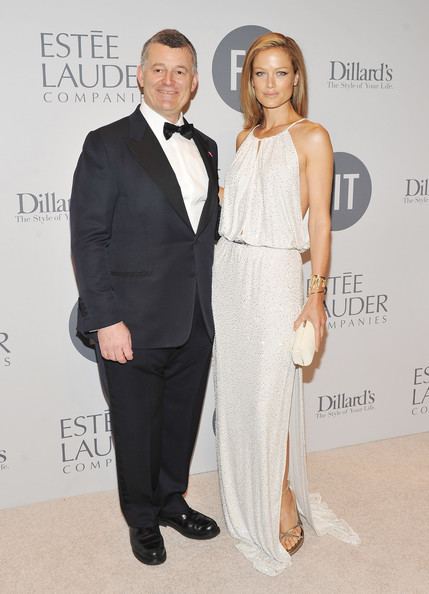 William P. Lauder and Carolyn Murphy are smiling and William is wearing a black coat, bow tie, pants, and white long sleeve while Carolyn is wearing a white sleeveless dress