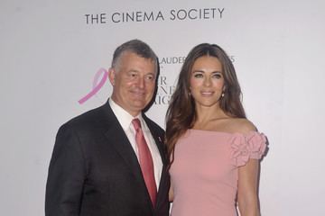 William P. Lauder and Elizabeth Hurley are smiling and William is wearing a black coat, white long sleeve, dark pink necktie while Elizabeth is wearing a pink dress