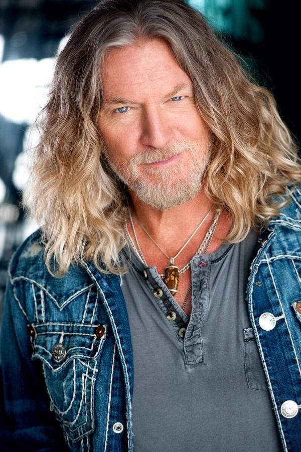 William Shockley posing with long hair and thicker facial hair and wearing a blue jean jacket over a gray shirt.