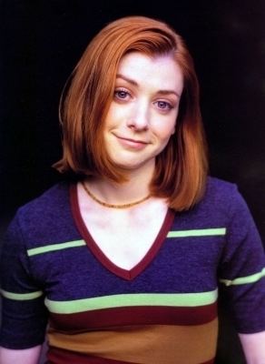 Willow Rosenberg smiling with short hair and wearing a v-neck blouse and a necklace
