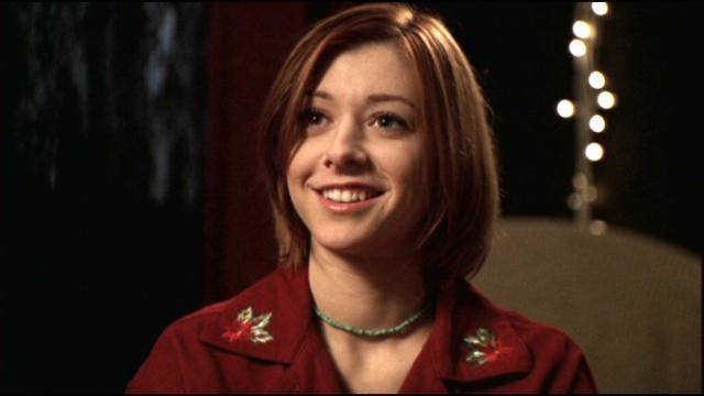 Willow Rosenberg smiling and wearing a red blouse with a beaded necklace in a scene from the 1992 film "Buffy the Vampire Slayer"