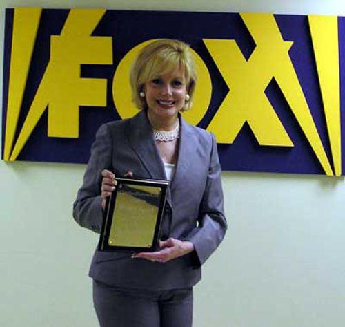 Wilma Smith smiling while holding an award she received and wearing a gray coat and pants